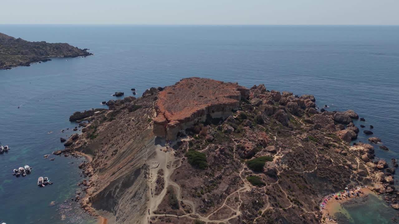 A rocky cliff plateau extends into the open sea, with rugged terrain and sparse vegetation. The elevated viewpoint highlights the natural coastline and the vast expanse of the ocean under a clear sky