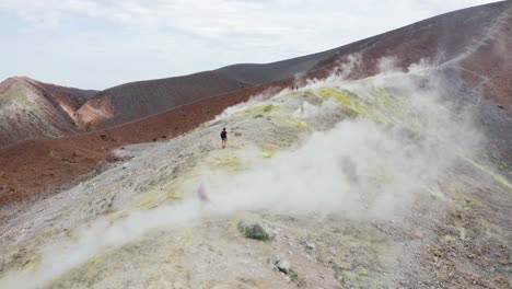 male and female hikers traveling trekking on volcano, walking trough sulfuric smokes.  volcano island travel destination in sicily, aeolian islands.