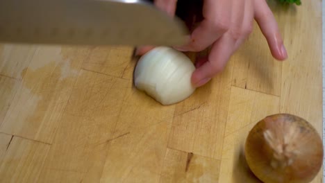 Manos-Femeninas-Cortando-Una-Cebolla-En-Una-Tabla-De-Cortar-De-Madera