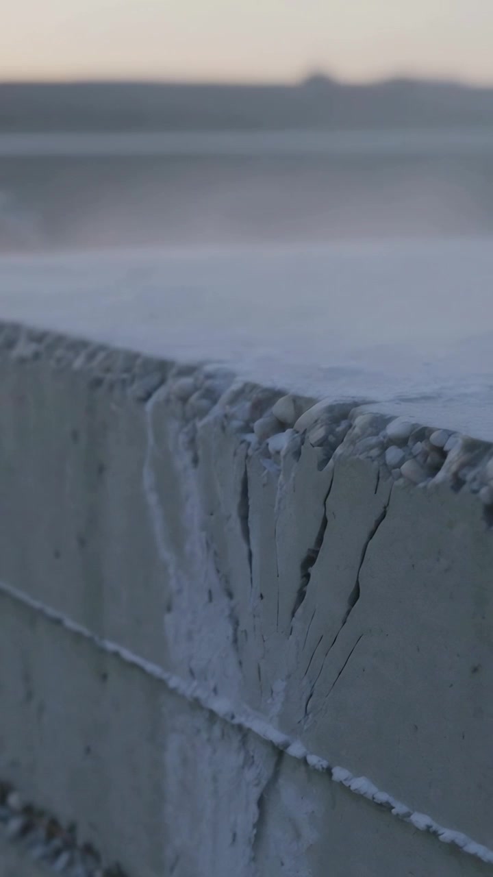 Vertical video: Shifting camera focusing on concrete seawall at coast revealing pebbles and salt