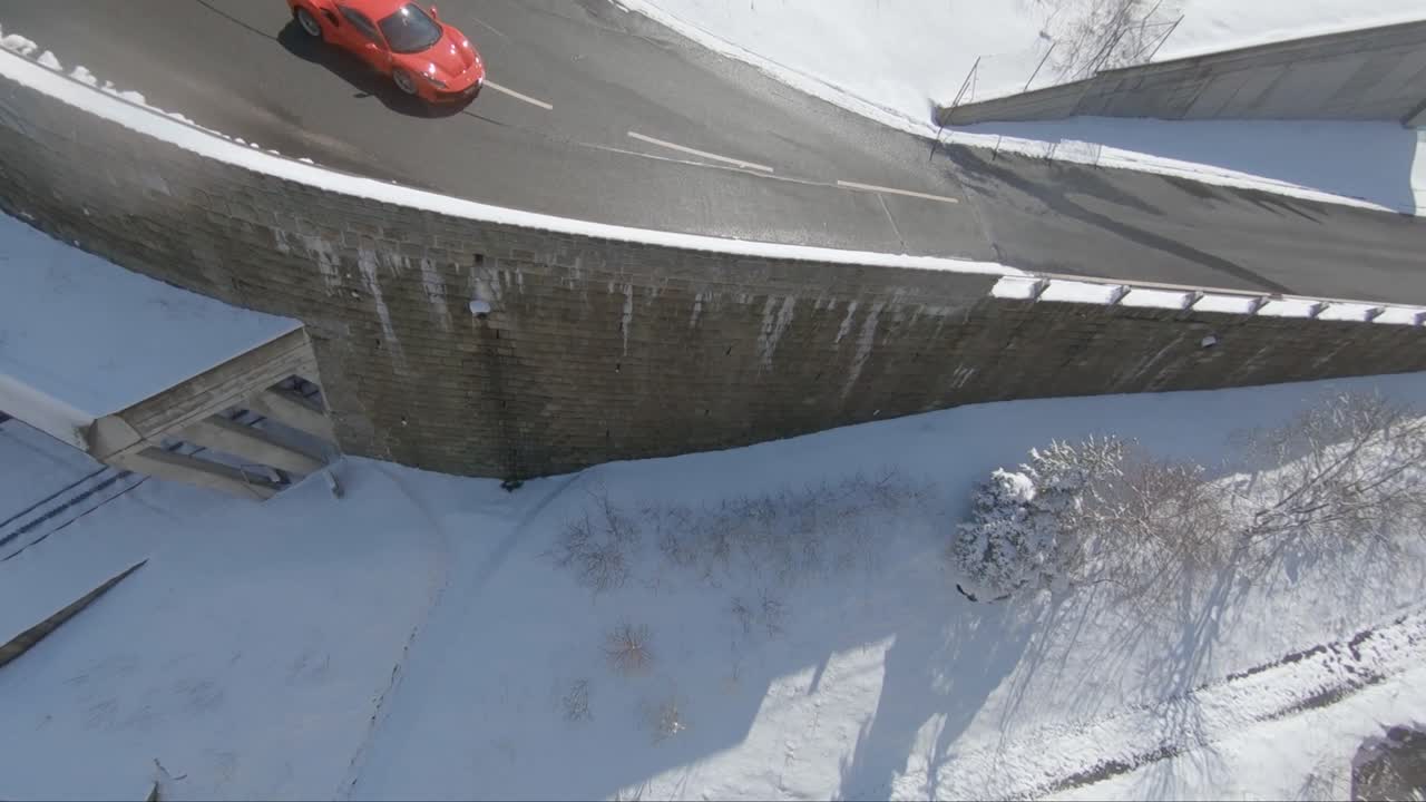 Sport drone view of Ferrari in the alps driving fast along a mountain road around curves