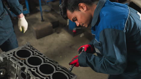 close-up of automotive engineer loosening a nut on engine block with red gloves, focused on precision in automotive workshop, with observer in white gloves standing nearby