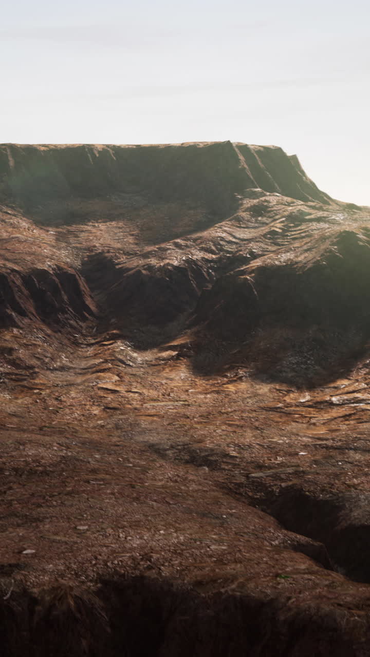 una gran cordillera rocosa se eleva hacia el cielo. las montañas son estériles y marrones, sin signos de vegetación. el cielo es de un azul pálido, y el sol brilla con brillantez. las montaña son una hermosa vista, y están seguros de inspirar temor en cualquiera que las vea.
