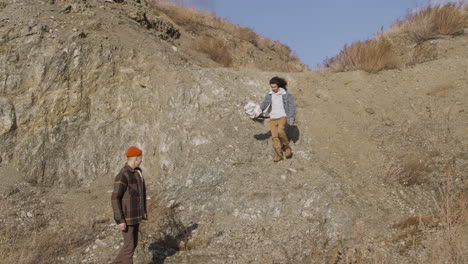 two teenage boys are talking and walking down a mountain path on a windy day