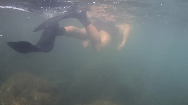 Person swimming below the surface of dark, murky water, showcasing exploration, freedom, and adventure. Sunlight creating ripples