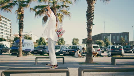 sportive girl holding skateboard crossing benches. woman waiting friend walking