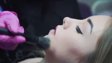 makeup for a girl in a beauty salon. the cosmetologist with a brush applies makeup powder on the face