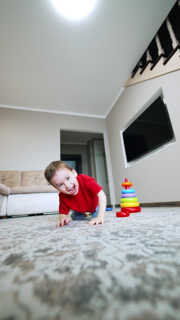 Happy baby boy plays at home. Cheerful toddler crawls by the floor approaching the camera. Vertical video.