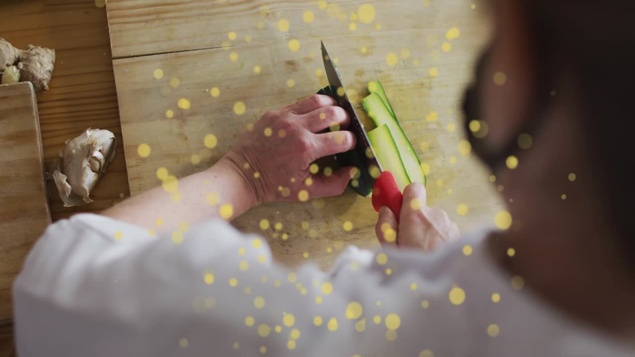 Chef placing halved zucchini on board, slicing with red knife for cooking, golden flecks drifting