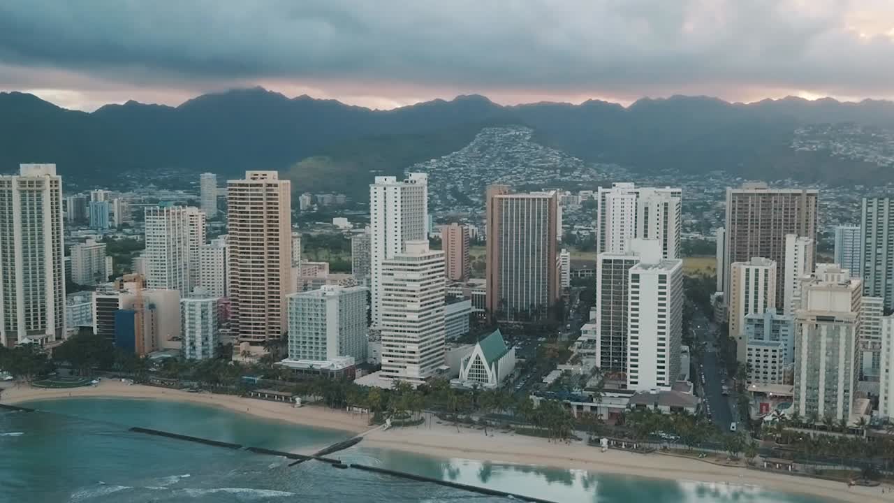 Drone aereo in lenta panoramica che sorvola lo skyline colorato di Honolulu al tramonto a Oahu, Hawaii, con la spiaggia di Waikiki come punto di interesse speciale