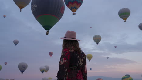 woman walking and admiring beautiful and majestic view of cappadocia with numerous air balloons in flight - medium shot