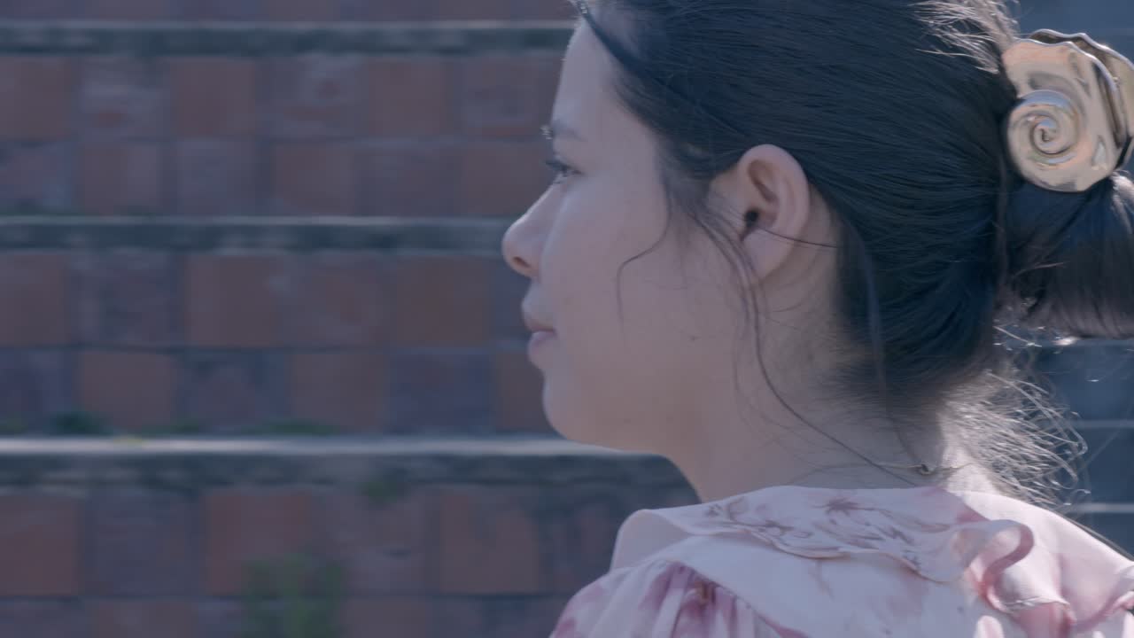 Close-up of a pensive woman in profile against a textured brick wall. Soft lighting captures her contemplative expression, creating an intimate and serene atmosphere