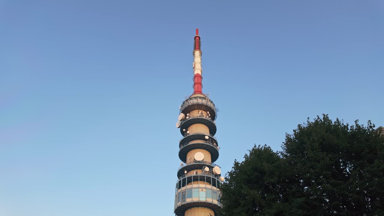 Kékestető TV Tower appears behind a tree against the clear blue sky before sunset in Hungary