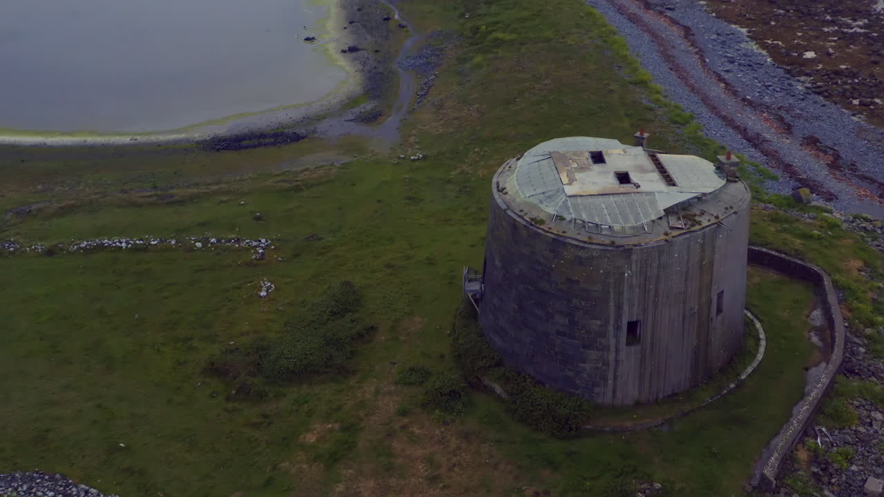 Aerial dynamic shot orbits and tilts down while tracking the top of Aughinish Martello Tower, revealing its architectural features. County Clare, Ireland
