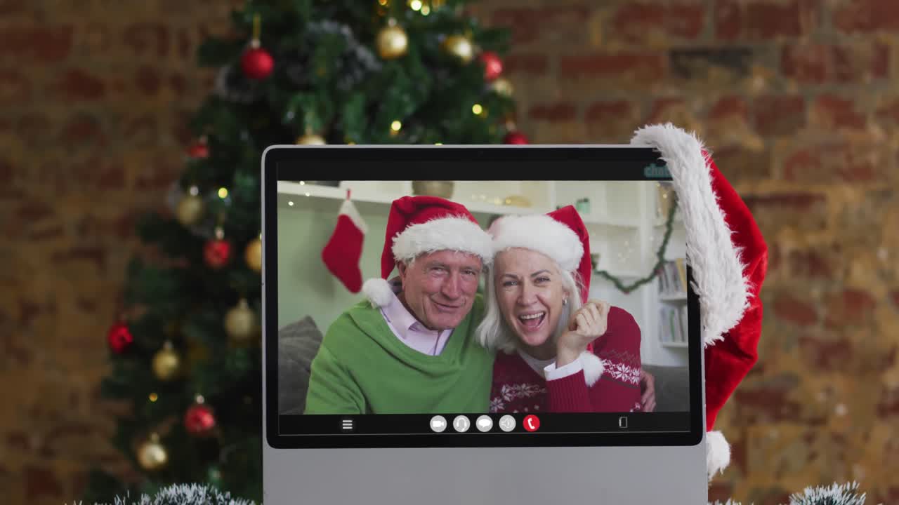 una pareja de alto nivel caucásica saludando en una videollamada en la computadora, con un árbol de navidad