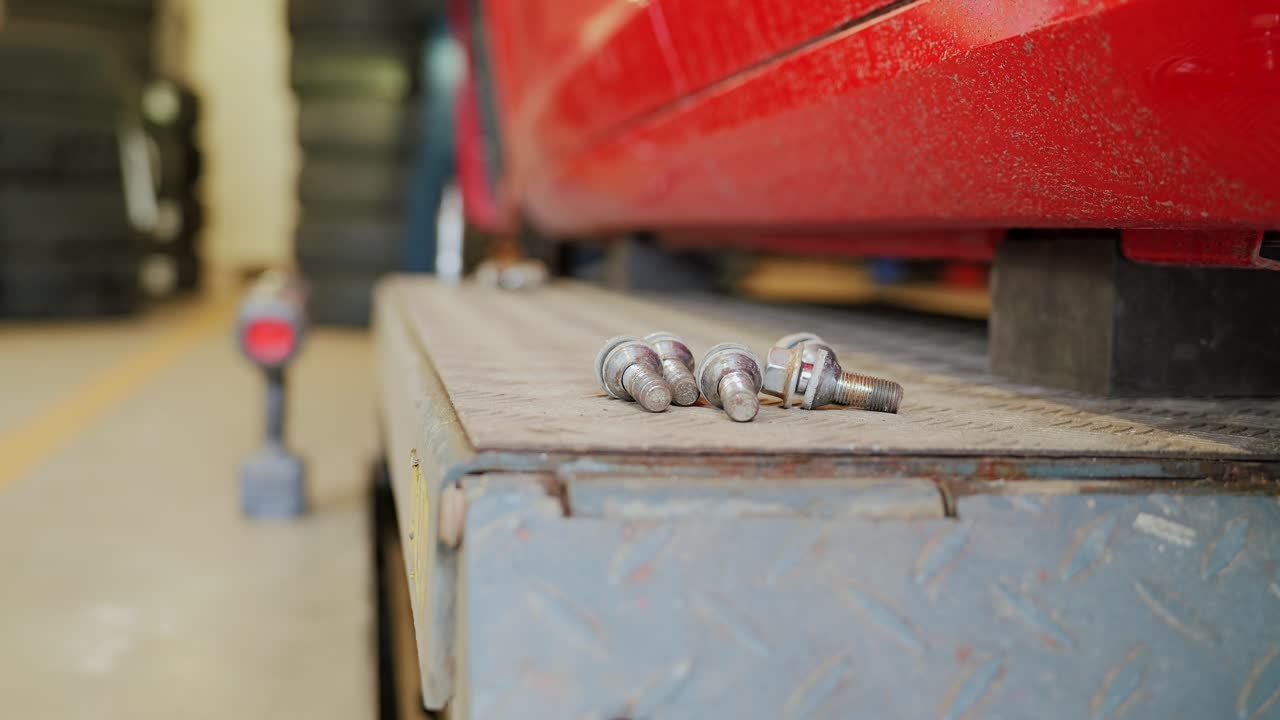 Wheel bolts scattered on metal platform with red car lifted for service in Riga