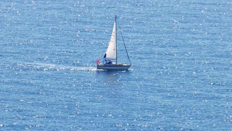 sailing yacht on wide blue sea reflecting sunlight, slow motion