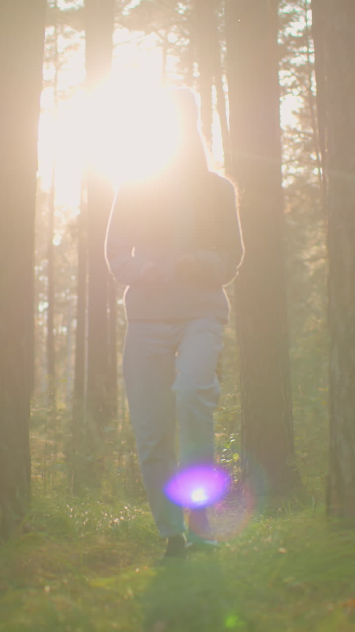joven con mochila camina a través de un bosque pacífico, bañado en la luz suave y cálida de la noche, su expresión pensativa mientras se mueve entre árboles altos y vegetación exuberante