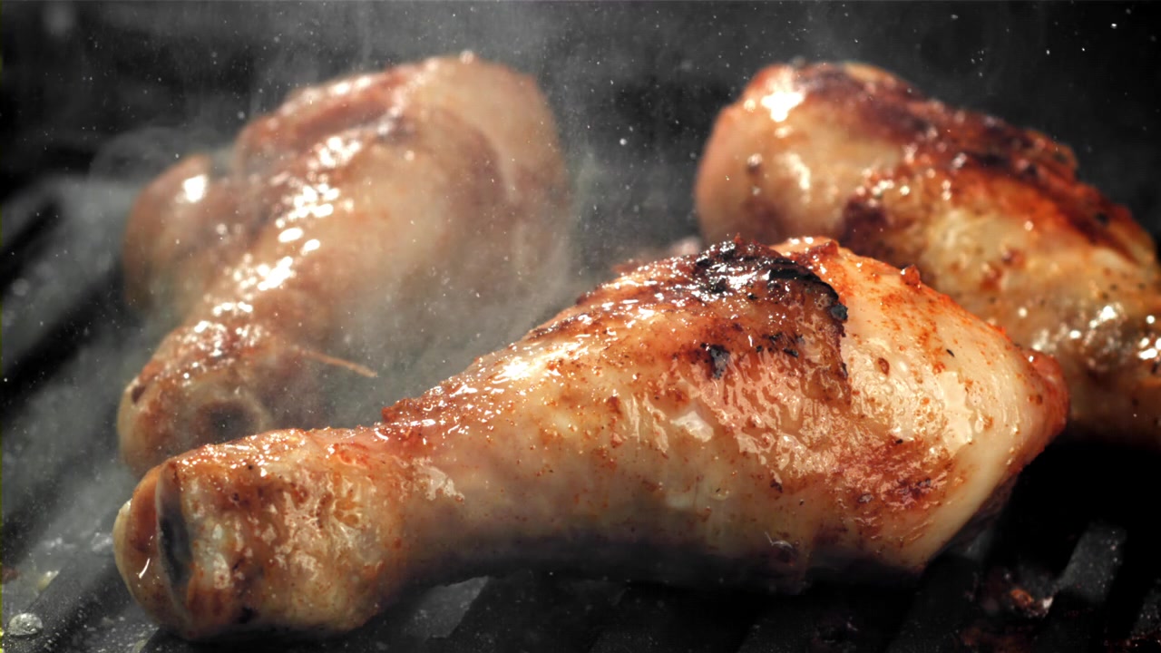Primo piano di fusi di pollo sfrigolanti che cuociono su una griglia rovente
