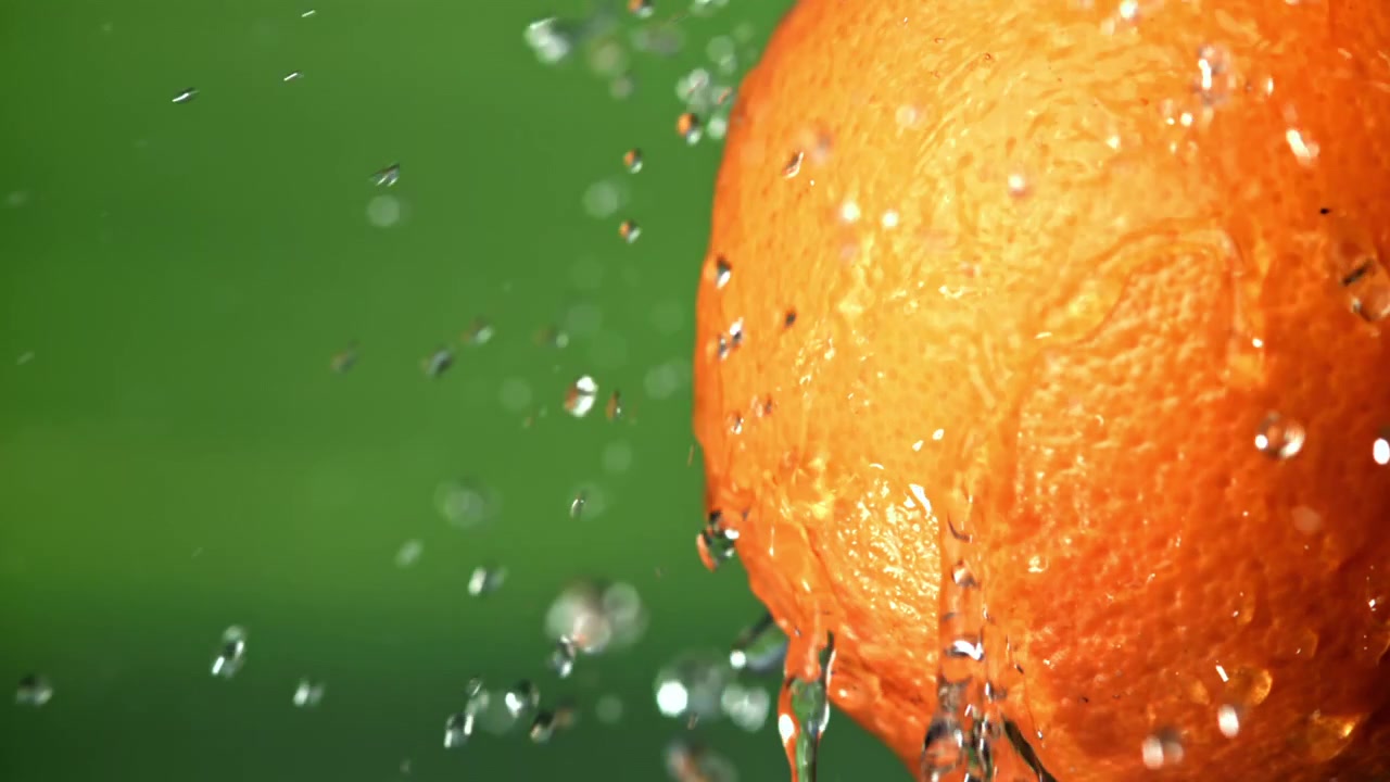 Zeitlupe: Wasserspritzer auf einer frischen Orange mit grünem Hintergrund