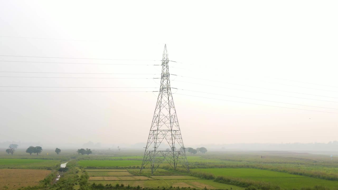 Forward moving vertigo aerial view towards electricity power pylon tower on misty Bangladesh meadow at sunrise