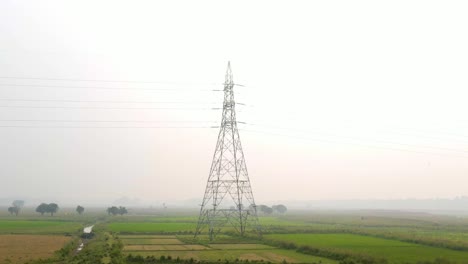 vista aérea de vértigo en movimiento hacia adelante hacia la torre del pilón de energía eléctrica en la pradera brumosa de bangladesh al amanecer
