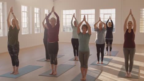 yoga class of healthy mature women practicing prayer pose enjoying morning physical fitness exercise workout in studio at sunrise