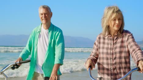 front view of active senior caucasian couple standing with bicycle on the beach 4k