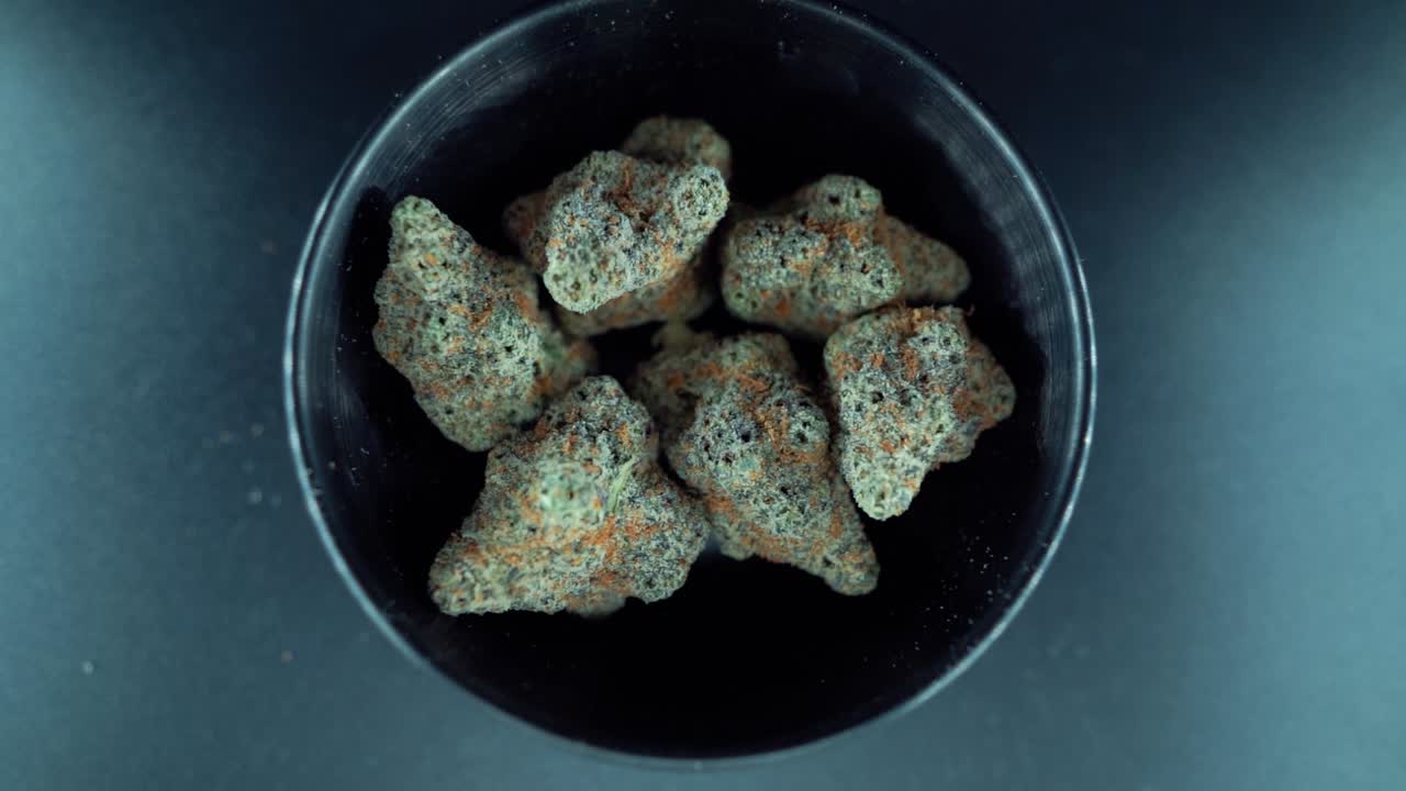 una macro cinematográfica de arriba hacia abajo zoom out movimiento suave de grúa toma de una planta de cannabis, cepas híbridas de naranja, tipo indica, flor de marihuana verde, cámara lenta 120 fps, luces de estudio, soporte brillante