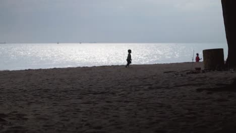 Silueta-De-Un-Niño-Pequeño-Corriendo-En-La-Playa-Con-El-Reflejo-De-La-Luz-Del-Sol-En-El-Fondo-Del-Mar