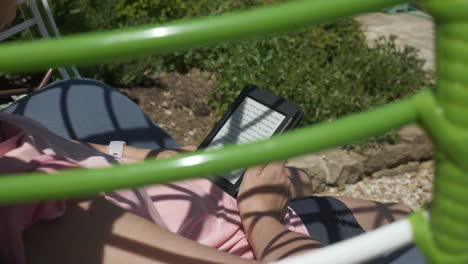 woman reads ebook novel relaxing in comfort garden furniture on sunny day