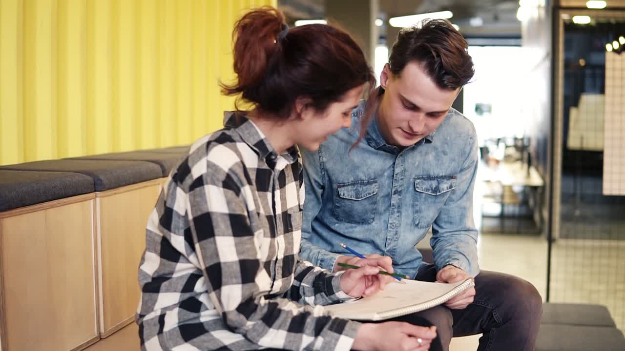 una linda pareja feliz dibujando algo en un bloc de notas. una atractiva chica morena está riendo, divirtiéndose con su novio.