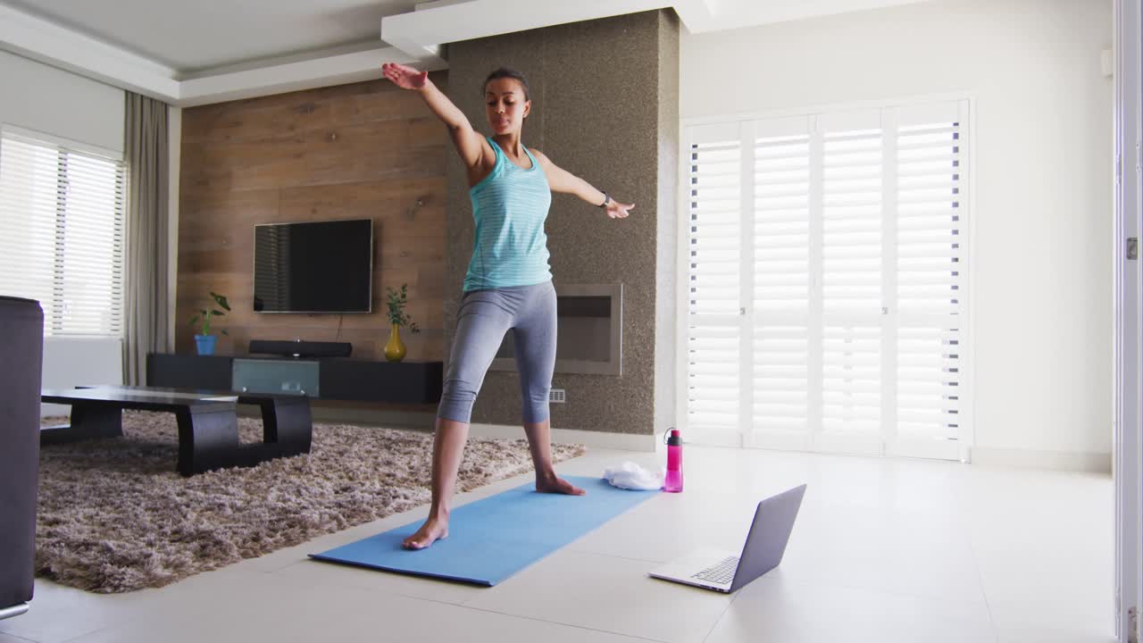 mujer de raza mixta haciendo ejercicio en una alfombra con computadora portátil