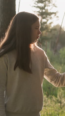 una mujer de pelo largo acaricia el tronco de un árbol en el bosque al atardecer. una joven camina tranquilamente bajo el suave resplandor del sol de la tarde. encontrando paz mental en la naturaleza