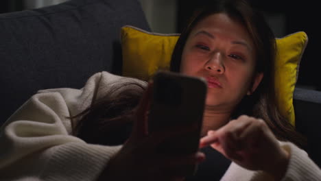 close up of woman spending evening at home lying on sofa with mobile phone scrolling through internet or social media 4