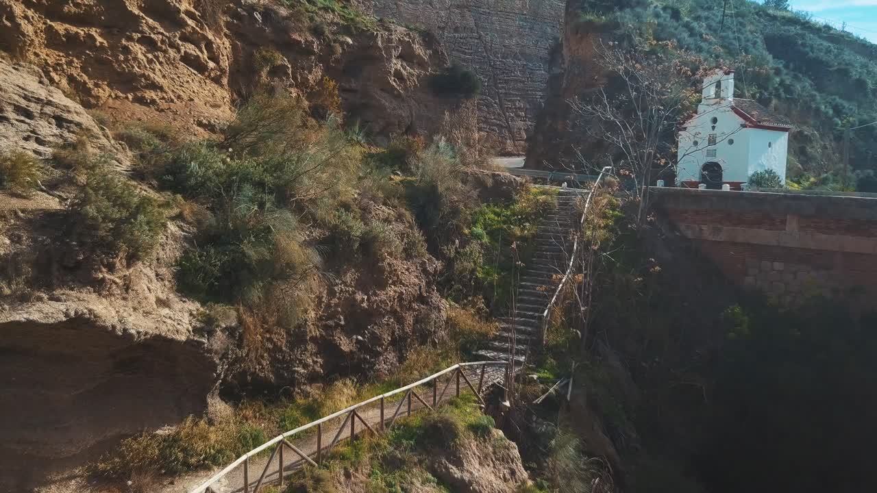 vista aérea de un sendero de senderismo que viene de un puente y una ermita católica sobre un barranco en españa