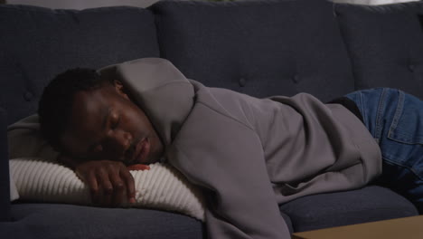 unhappy and depressed young man lying on sofa at home looking anxious and worried at night