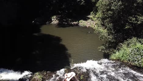 Drone-aerial-in-nature-with-a-woman-standing-on-the-ledge-of-a-waterfall-camera-panning-down