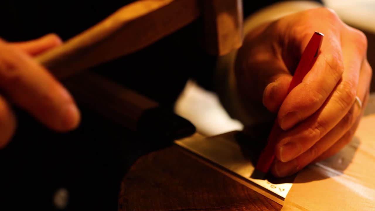 Close-up of hands using a hammer and chisel on a metal surface with focused precision.