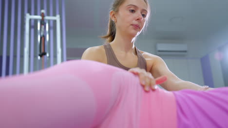 gym instructor attentively monitors lady in pink performing workout in well-lit gym with stylish decor, guiding her through exercise for strength, endurance, and flexibility