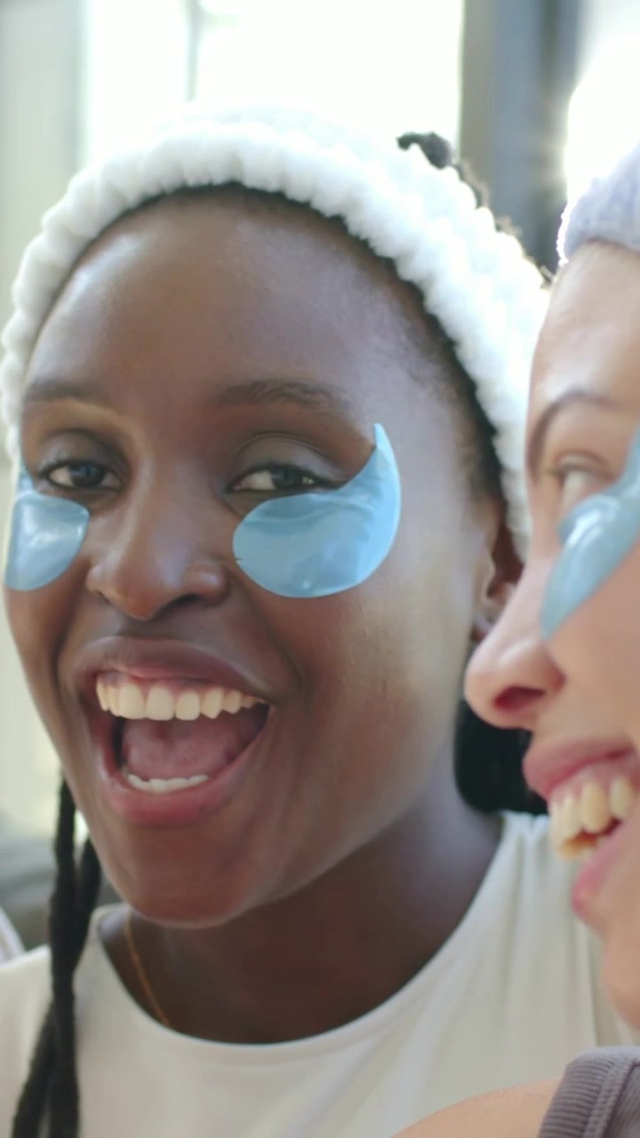 Vertical video: Cam recording woman white headband speaking, laughing at home with blue gel patches