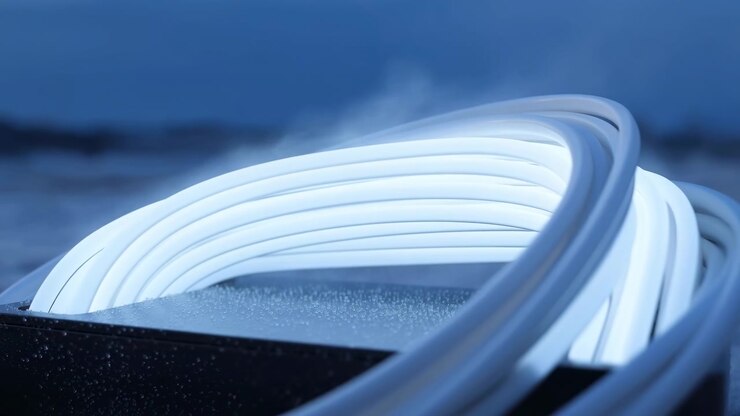 Primo piano di un cavo bianco arrotolato che poggia su una superficie scura sotto una soffusa illuminazione blu, creando una composizione astratta minimale con profondità di campo ridotta e un