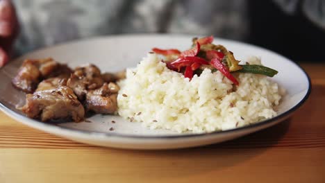 Close-up-of-woman's-hand-using-fork-to-take-fried-meat-from-her-plate-filled-with-rice.-Lunch-in-cafe