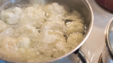 cauliflower boils in a metal pot over a white covered stove