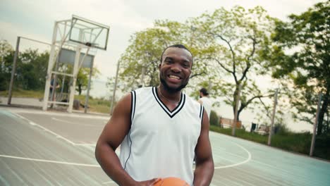 Black-man-smiling-broadly,-posing-and-showing-his-emotions-while-playing-basketball-on-the-basketball-court-with-his-friends-in-summer