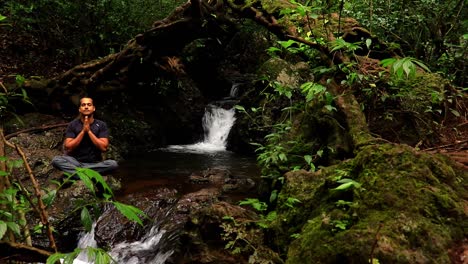 hombre meditando en la cubierta de la cascada con clip de ángulo plano de bosque exuberante verde