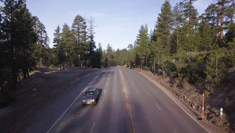 dark suv truck drives alone down a four-lane highway through a dense pine forest in the late afternoon