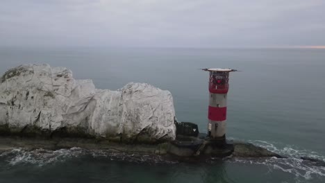 aerial drone flight around the red and white lighthouse at the needles in the isle of wight showing a detailed view of the white cliffs and waves crashing against the rocks