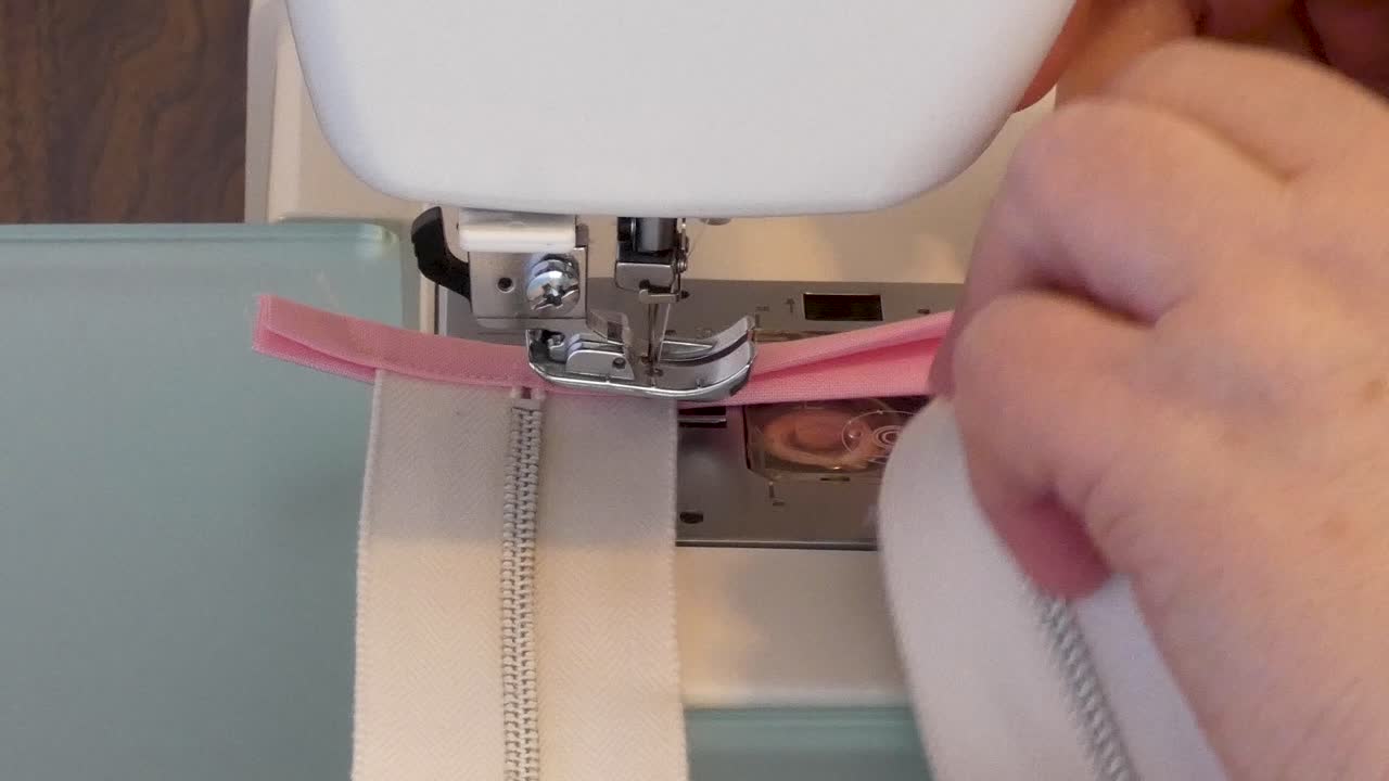 A woman sews fabric stops at ends of metal zippers.