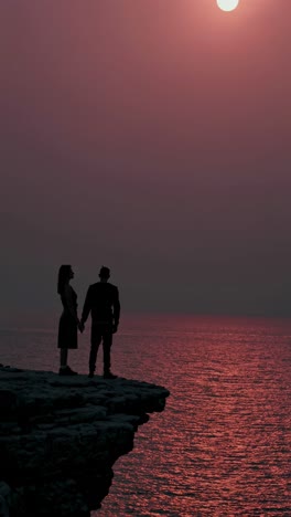 una pareja en un acantilado al atardecer.